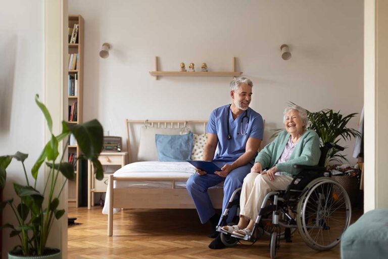 An elderly woman sits at a table with her adult daughter, discussing paperwork together in a home-like setting.