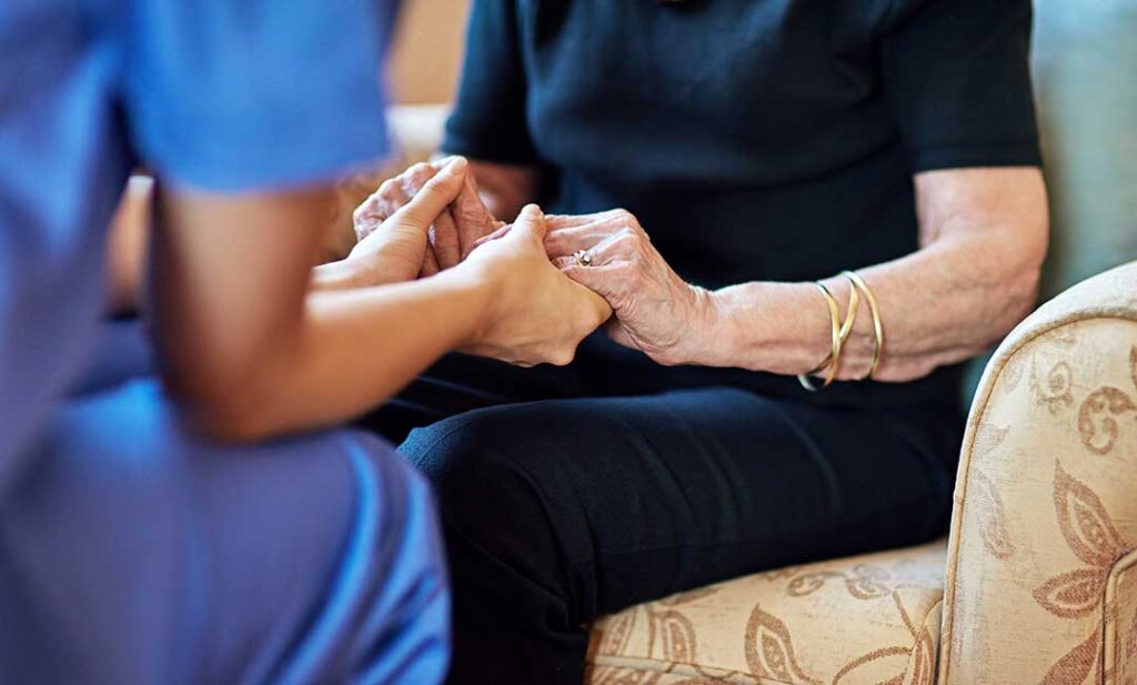 An older adult sitting thoughtfully at a kitchen table with concerned family members nearby.